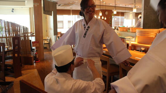 Katina with her arms spread out as she is being fitted for a sushi chef robe. 