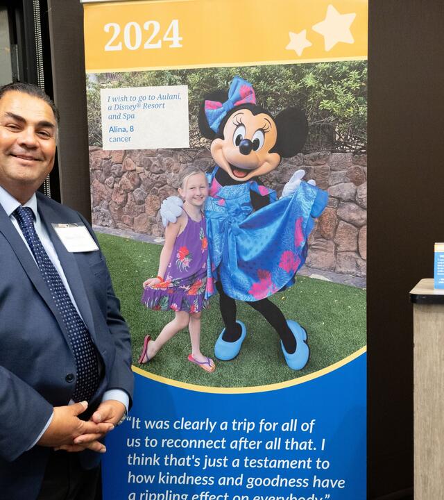 Volunteer John Villanueva at Wish Insiders Monterey standing next to a popup sign for Make-A-Wish Greater Bay Area's first wish