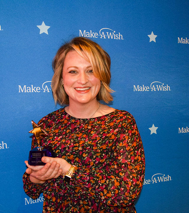Angela holding a trophy in front of a Make-A-Wish Banner