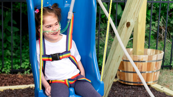 Make-A-Wish Eastern North Carolina's 5000th wish kid, Addie, smiles in her new swing that was part of her wish to have an adaptive playset.