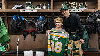 Cameron holding up a custom jersey next to Marc Fleury in the Wild locker room