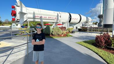 a boy standing in front of a large rocket, smiling