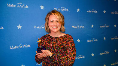 Angela holding a trophy in front of a Make-A-Wish Banner
