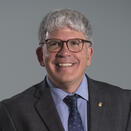 A man smiling with a suit and tie. He is wearing glasses.