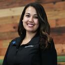 Tori wears a black Make-A-Wish zip up and stands in front of a wooden paneled wall.
