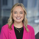 Woman smiling. She has shoulder length blonde hair. She is wearing a pink jacket.
