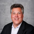 Neil Liebman smiling and wearing a white shirt with black suit jacket