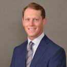 Graham Williams headshoot, man in blazer on grey background 