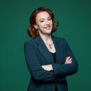 Woman smiling with arms folded in front of green background 