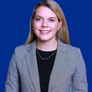Madison Lawson headshot, woman in grey blazer and black shirt on blue background