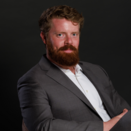 Win Loeb headshot, man sitting in chair wearing grey suit