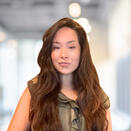 An Asian woman smirking with long brown hair. She is wearing a frilly dark green blouse.
