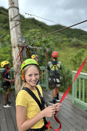 Nora wearing a helmet and protective equipment on the top of a tropical hill getting ready to zipline