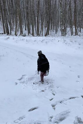 Wish kid Kayden running in the snow. He's facing away from the camera wearing a black snowsuit